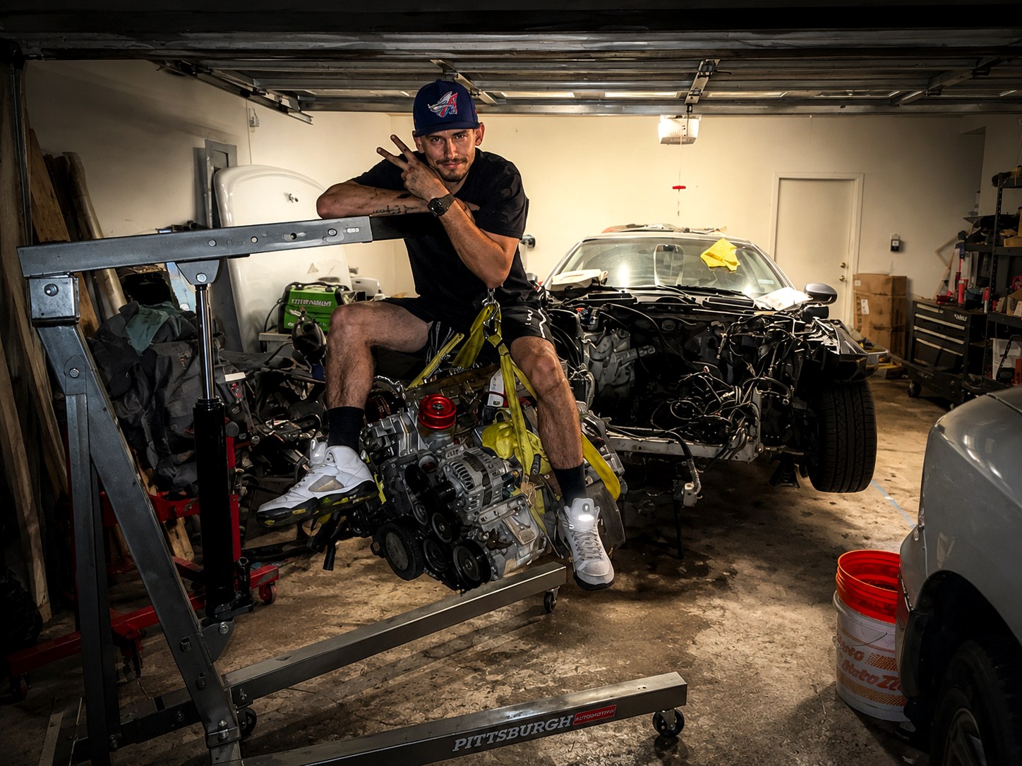Tom from Tom's Garage sitting on an engine attached to a hoist
